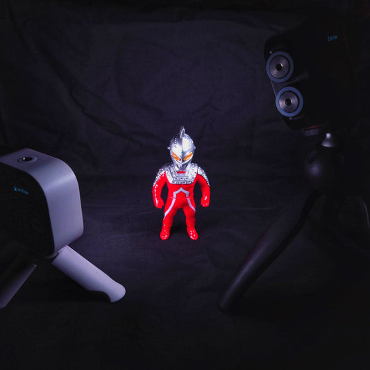 Red and silver robot figurine spotlighted in a dark room, surrounded by cameras.