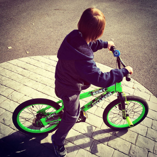 Young boy enjoying a ride on a bright green bicycle on a sunny day outdoors.