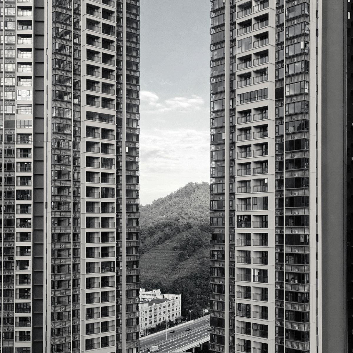 Tall urban buildings framing a scenic view of hills and sky in black and white.
