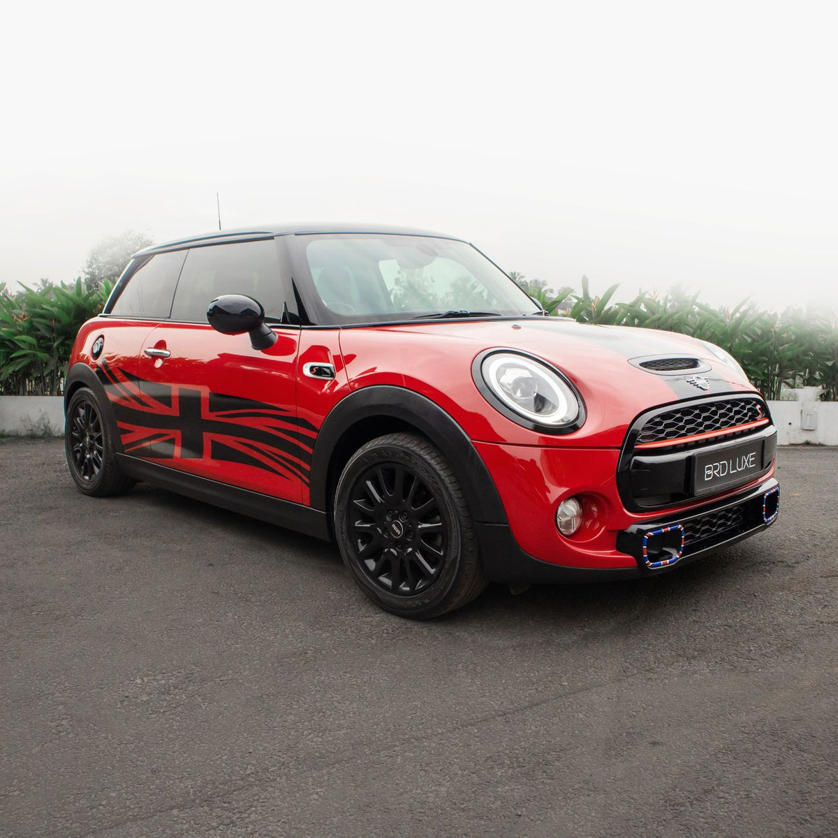 Red Mini Cooper with a Union Jack decal parked on a pavement, featuring stylish black wheels and a sleek design.