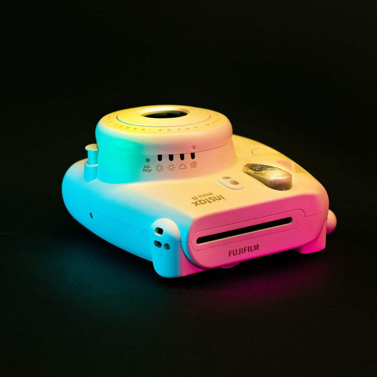 Close-up of a Fujifilm Instax Mini 8 instant camera with vibrant lighting on a dark backdrop.