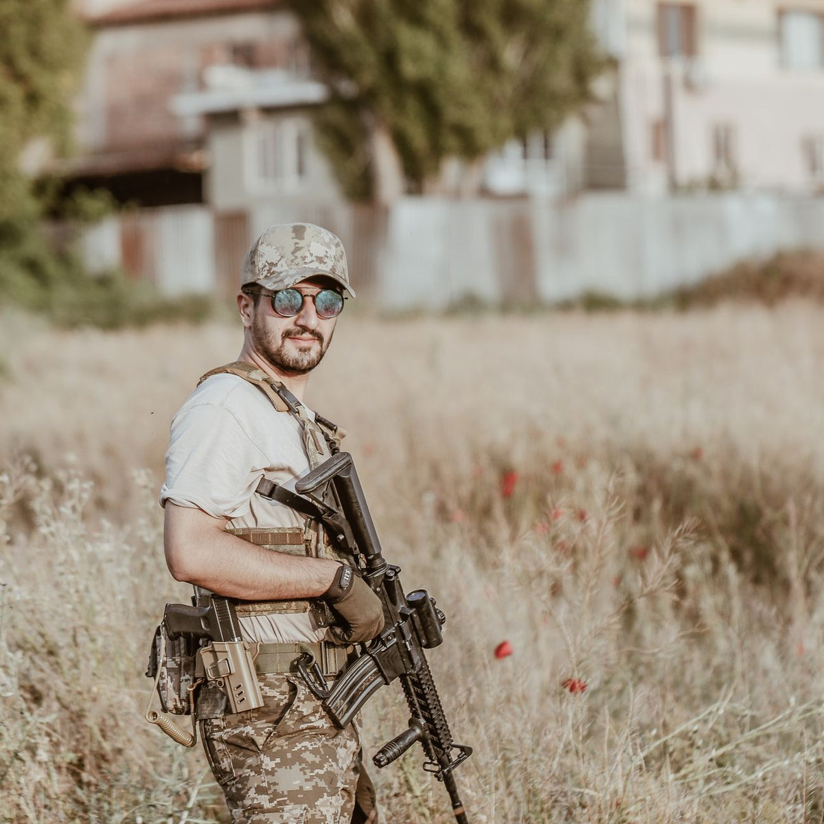 Soldier in camouflage attire with rifle posing outside in a field, showcasing military presence and readiness.