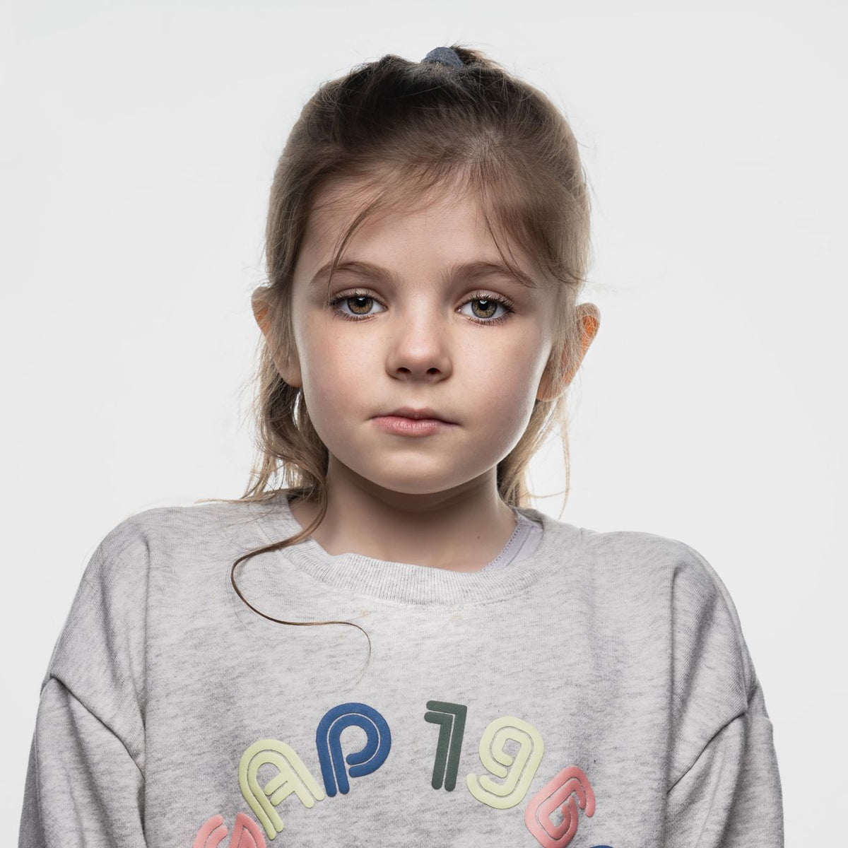 A thoughtful portrait of a young girl in a casual sweatshirt on a white background.