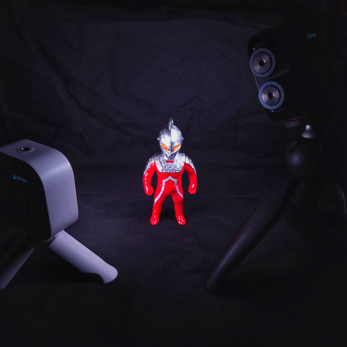 Red and silver robot figurine spotlighted in a dark room, surrounded by cameras.