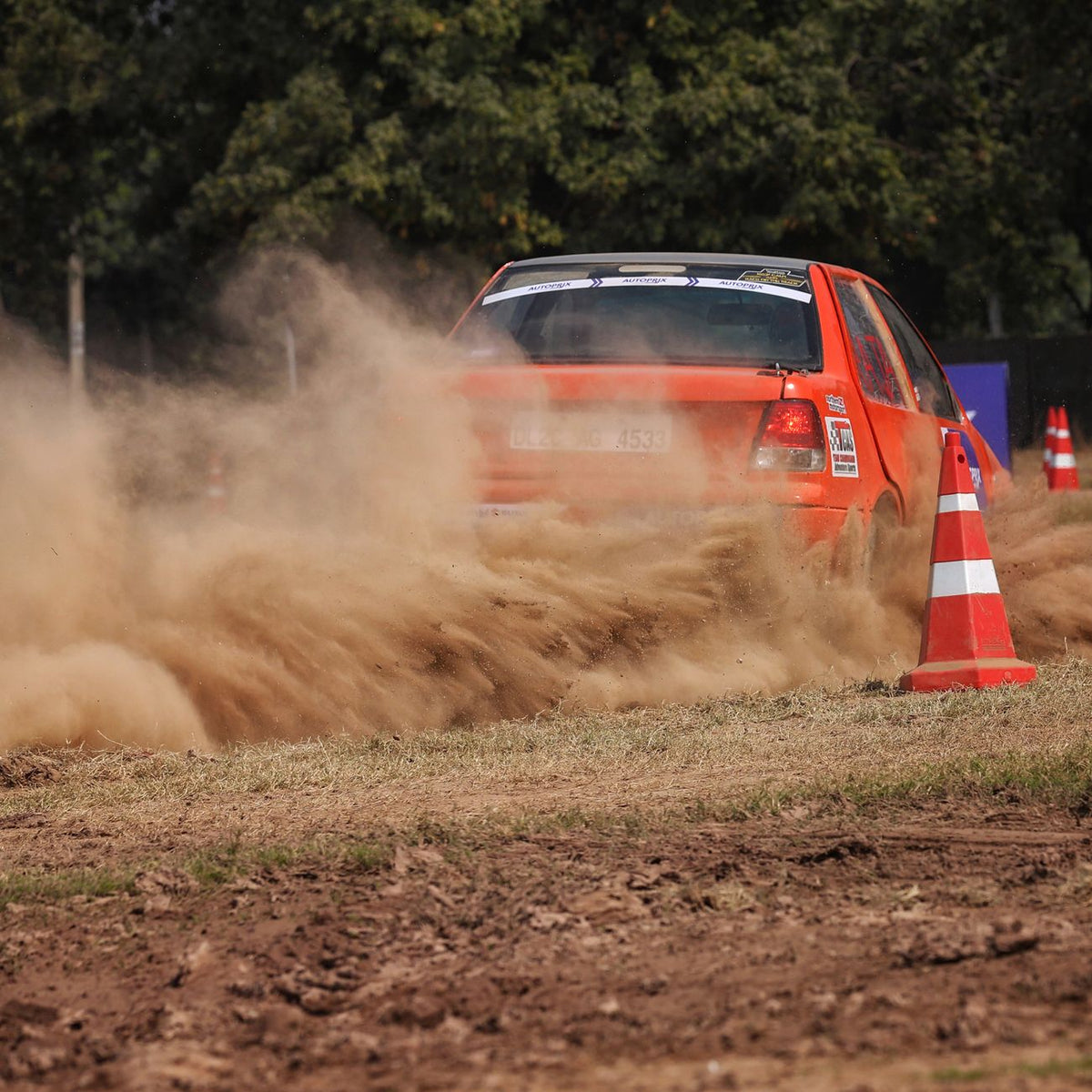 Orange rally car speeding through a dusty track, leaving trails of dirt. Perfect for motorsport themes.