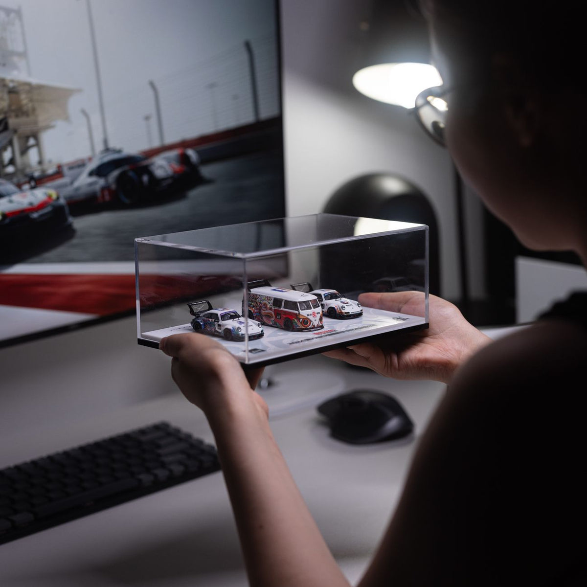 A person holds a display case with model cars in a stylish workspace.