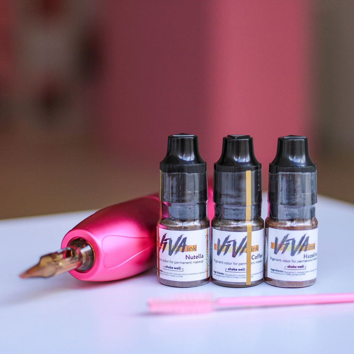 Set of tattoo ink bottles with a pink rotary machine and brush on a table.