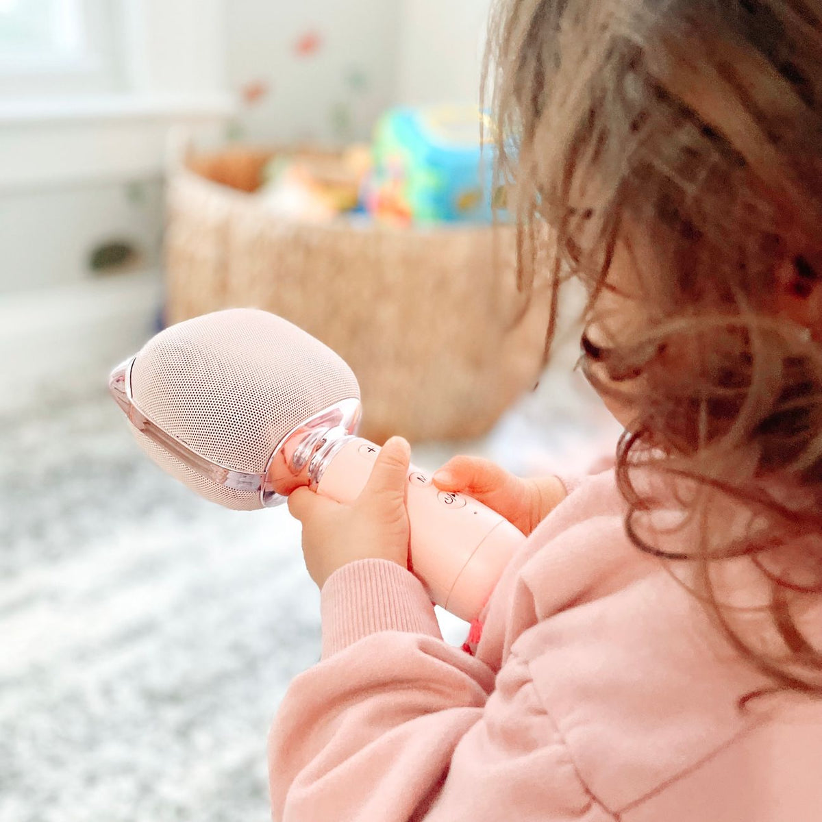 A child holds a pink toy microphone, singing happily indoors in a cozy setting.