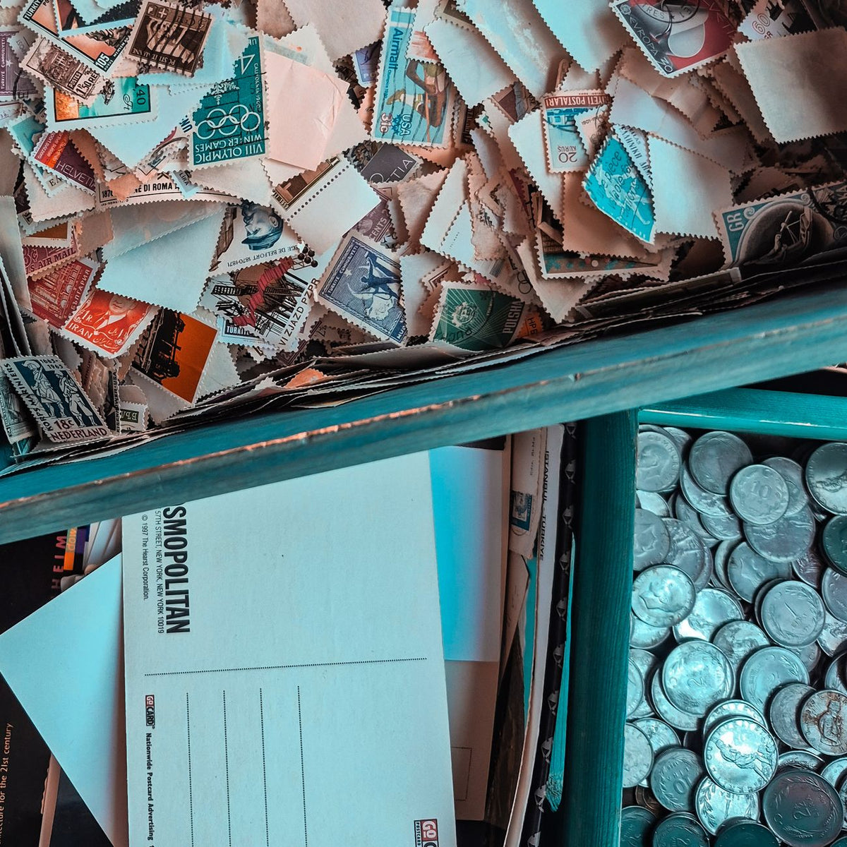 Top view of vintage stamps, postcards, and coins in a collector's box, showcasing nostalgia.