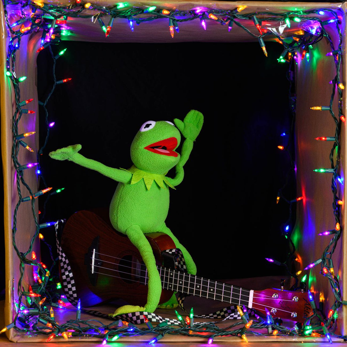 Kermit the Frog toy in a box with colorful lights and a ukulele, showcasing a festive and playful setting.