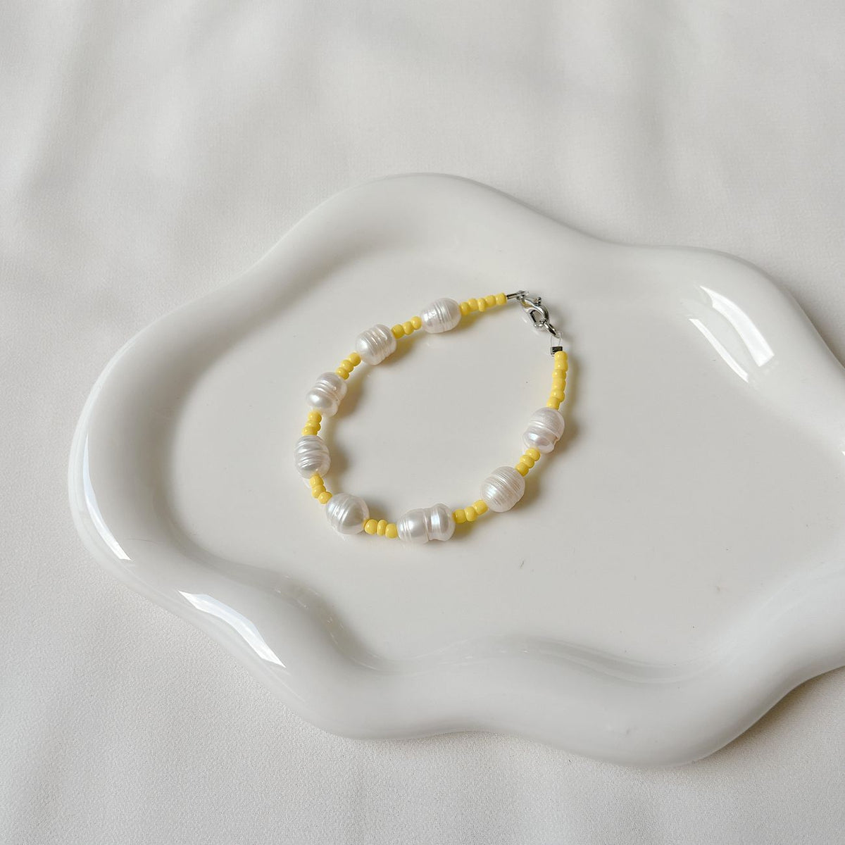 Stylish bracelet with pearls and yellow beads displayed on a decorative white plate.