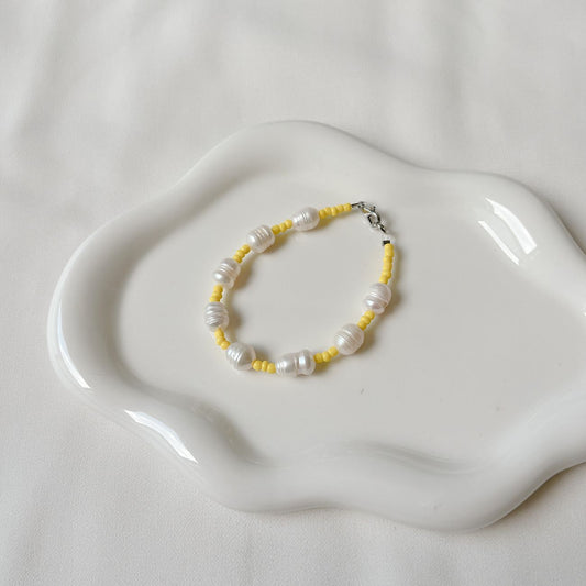 Stylish bracelet with pearls and yellow beads displayed on a decorative white plate.