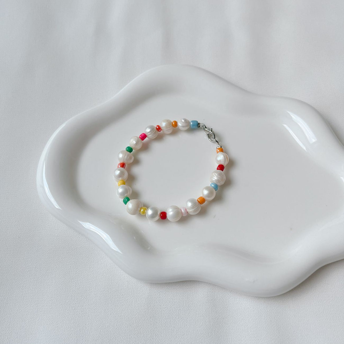 A vibrant bracelet with pearls and colorful beads elegantly placed on a white ceramic plate.