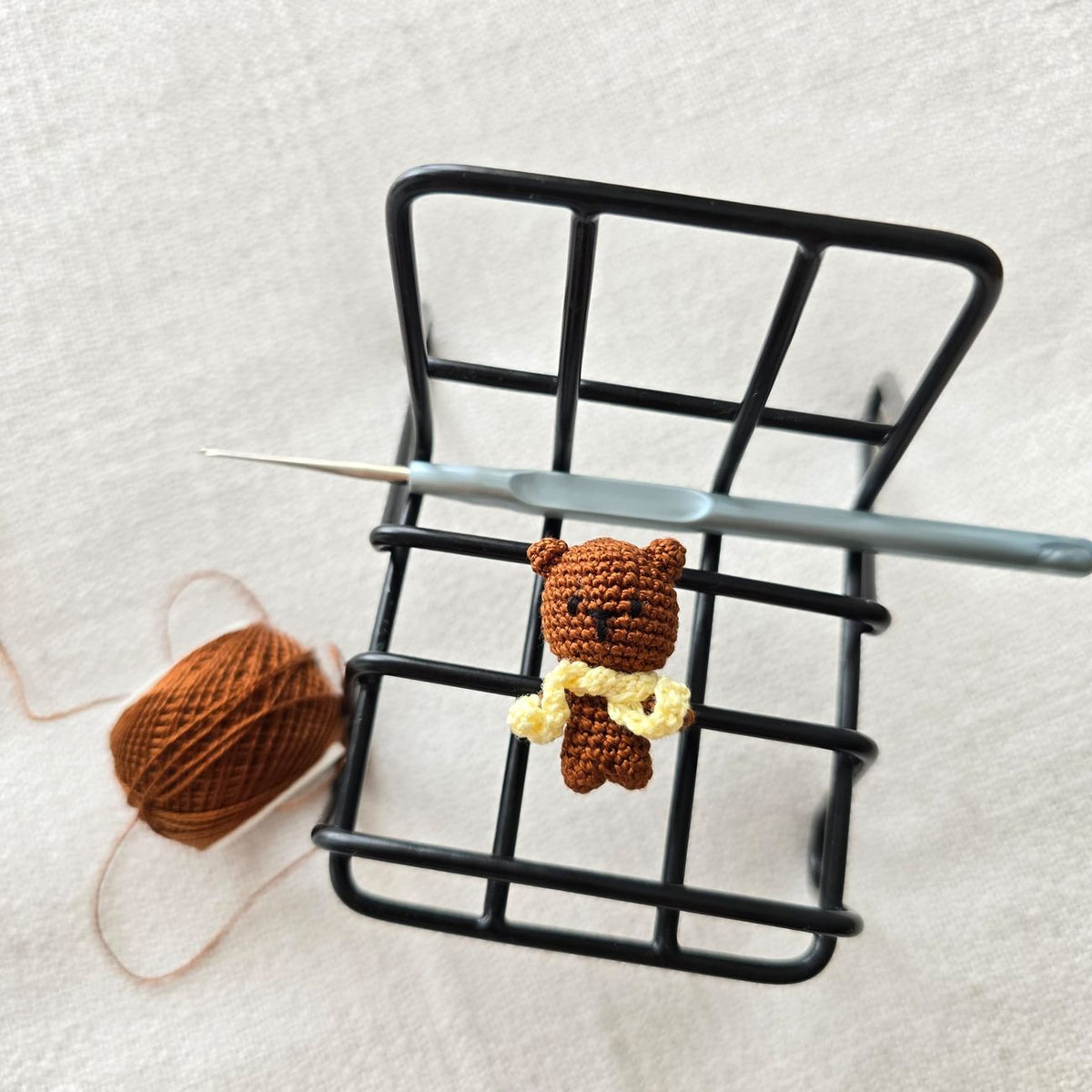 Cute crochet bear with yarn and hook on metal rack, perfect for craft enthusiasts.