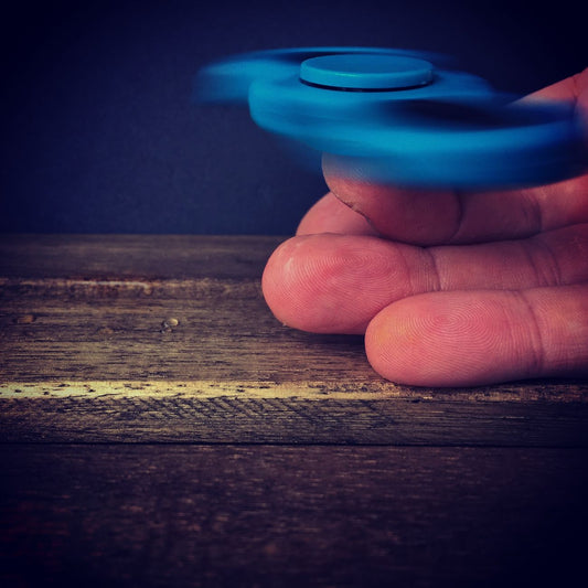 Close-up of a person spinning a blue fidget spinner on a wooden surface.