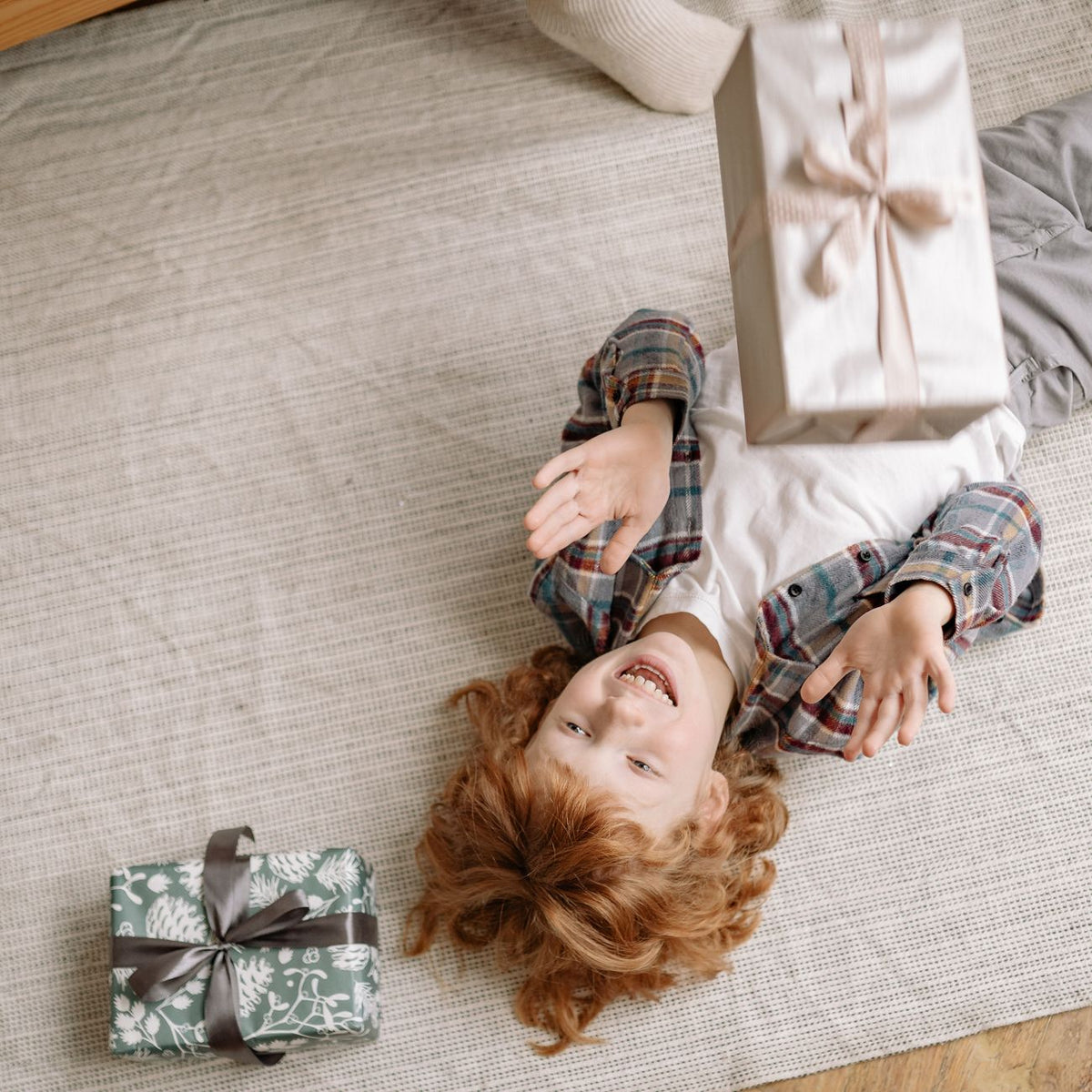 A happy child plays with gifts indoors, capturing an overhead playful moment.