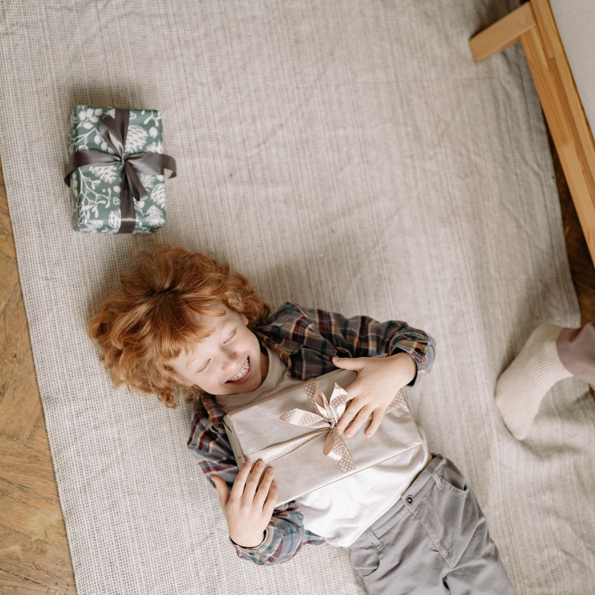 Happy child lying on floor holding gift, smiling joyfully indoors. Perfect for festive themes.