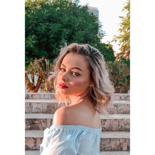 A fashionable woman poses outdoors with an off-shoulder blouse, exuding a confident and stylish vibe.