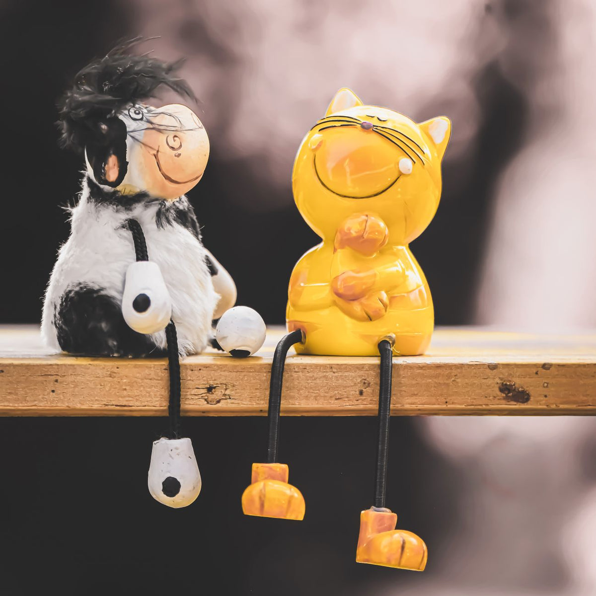 Charming cat and cow figurines sitting on a wooden shelf, captured with selective focus and bright colors.
