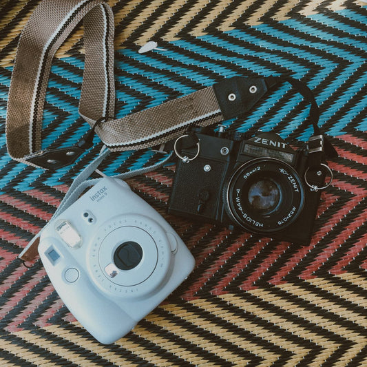 A vintage Zenit camera and a modern Instax camera placed on a woven colorful mat.
