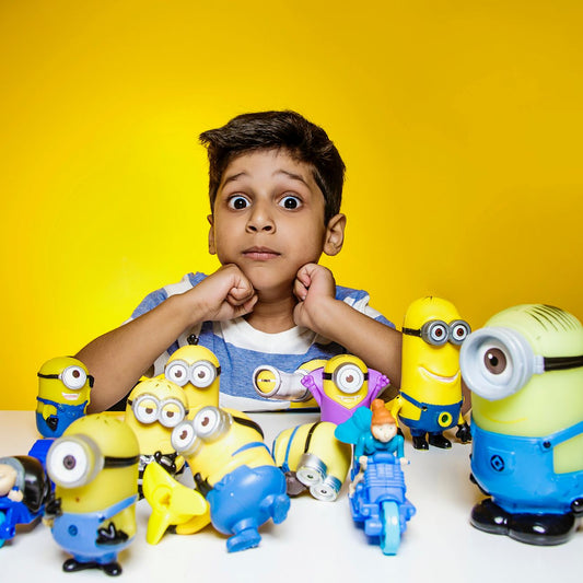 Young boy visibly excited with Minion toys in front against a vibrant yellow background.